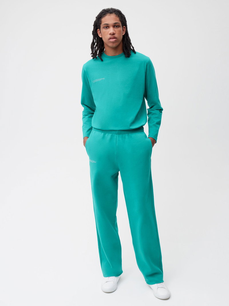 Man wearing a teal long-sleeve crewneck sweatshirt with embroidered planet details.