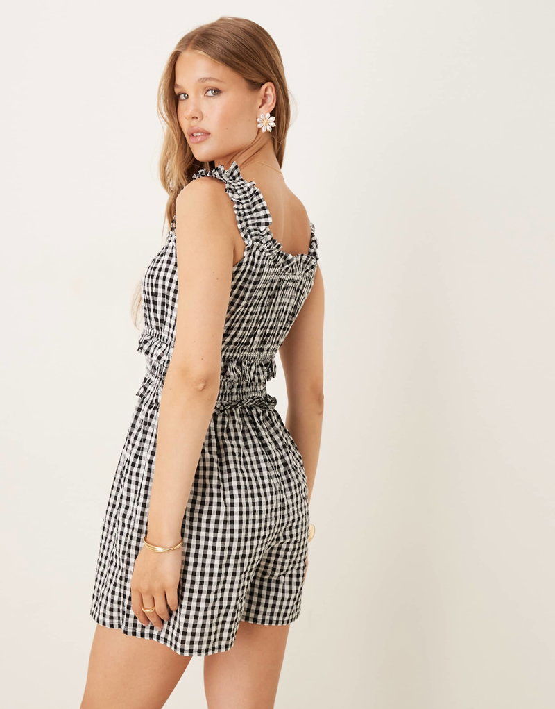 Black and white gingham romper with a tie waist, worn by a model.