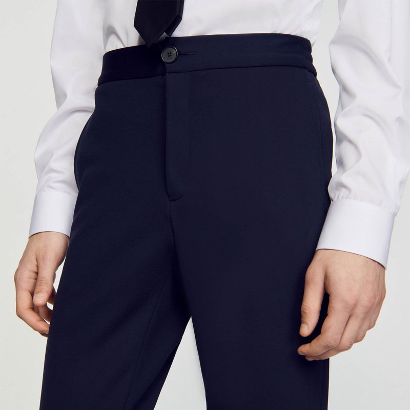 Dark navy trousers with a high waist and a buttoned cuff, worn with a white shirt.