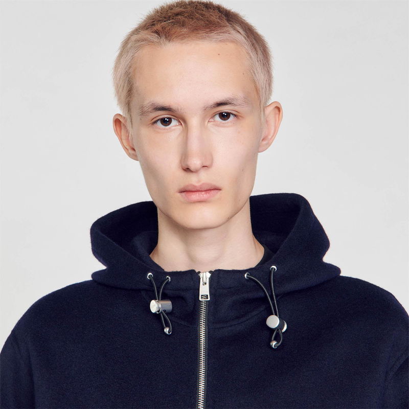 SANDRO - Young man wearing a dark grey hooded sweatshirt with silver drawstrings.