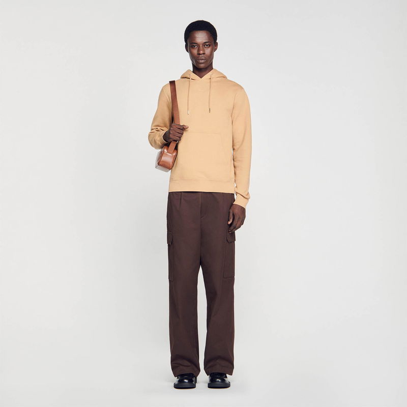 Man wearing a beige hoodie and brown cargo pants with a crossbody bag.