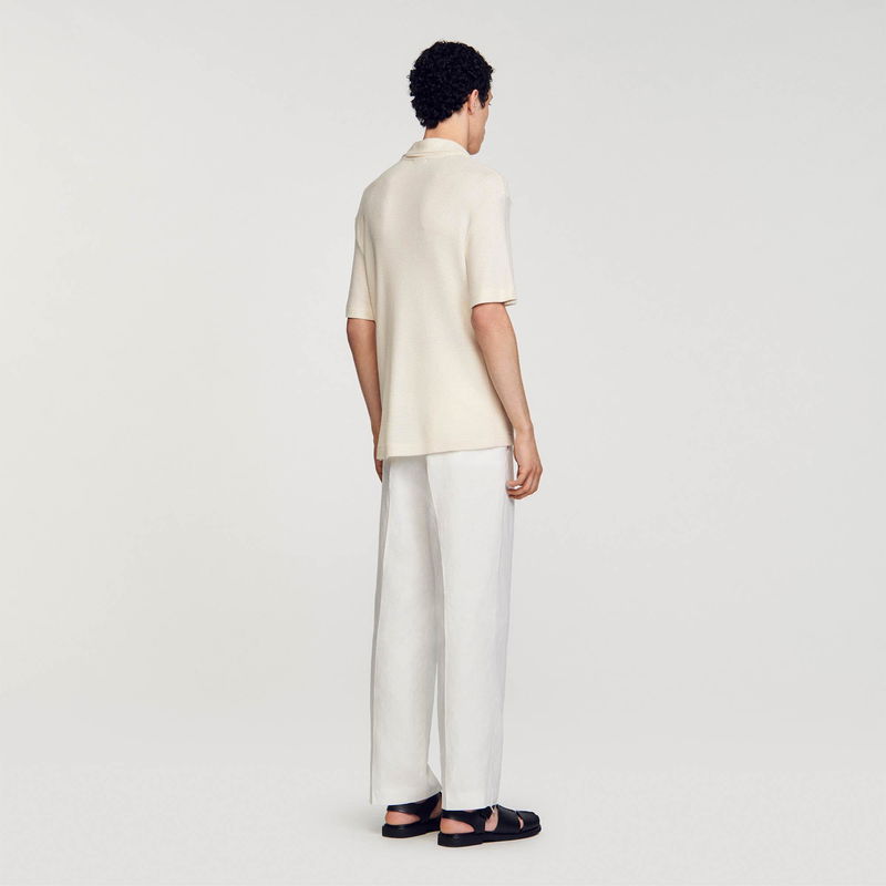 Sandro – man wearing a textured cream-colored knit shirt and linen trousers.