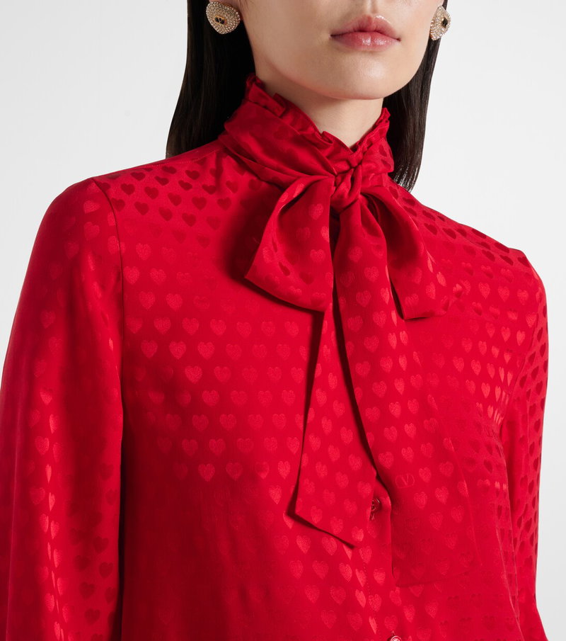 Red satin blouse with heart pattern and bow tie, worn by a woman.