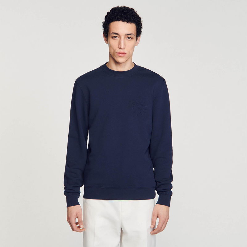 Man wearing a navy sweatshirt with an embossed floral design.
