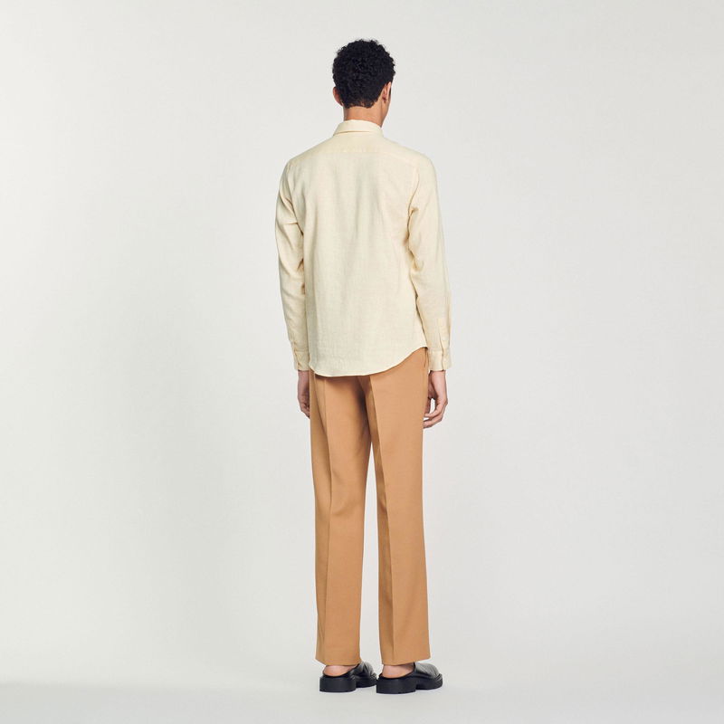 Sandro – Man wearing a beige linen shirt and brown trousers.