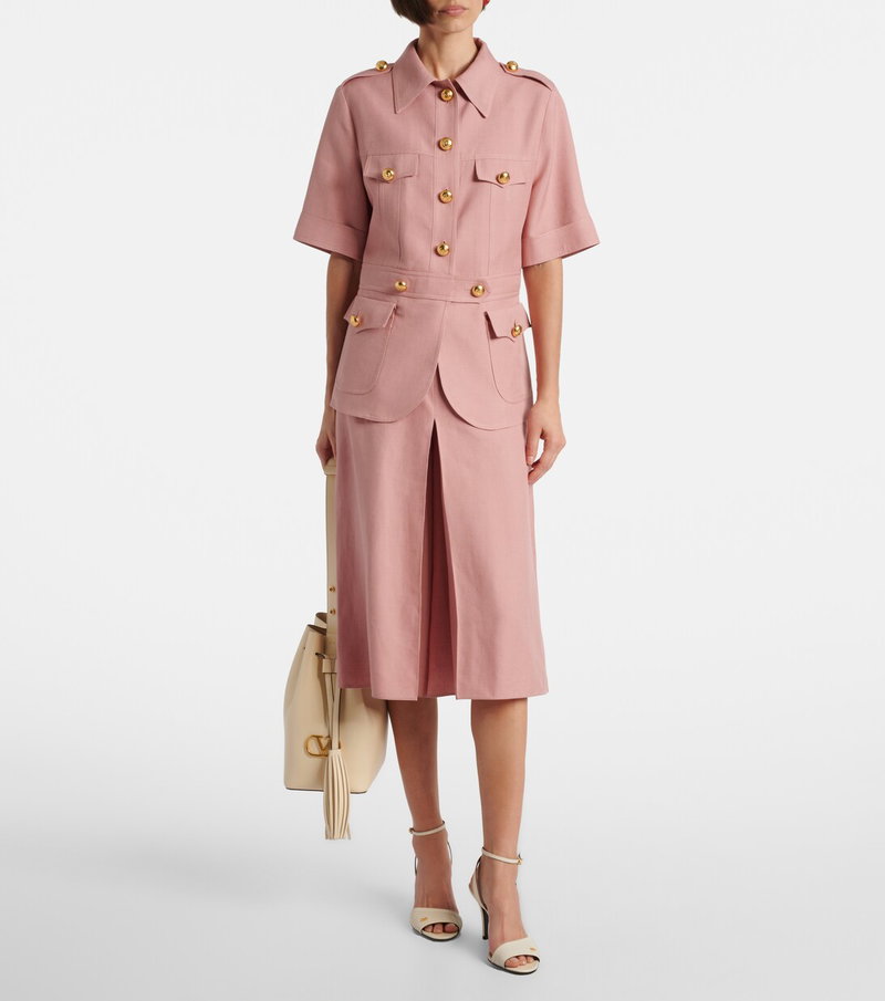 Pink Valentino safari-style jumpsuit with gold buttons and a beige handbag.