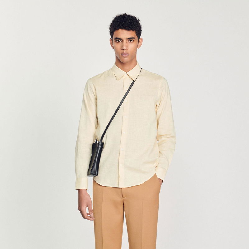 Man wearing a cream linen shirt with a black crossbody bag.