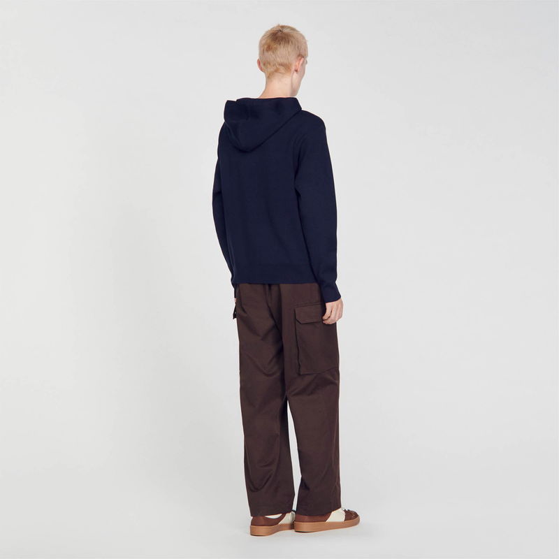 Man wearing a navy hooded sweater and brown trousers