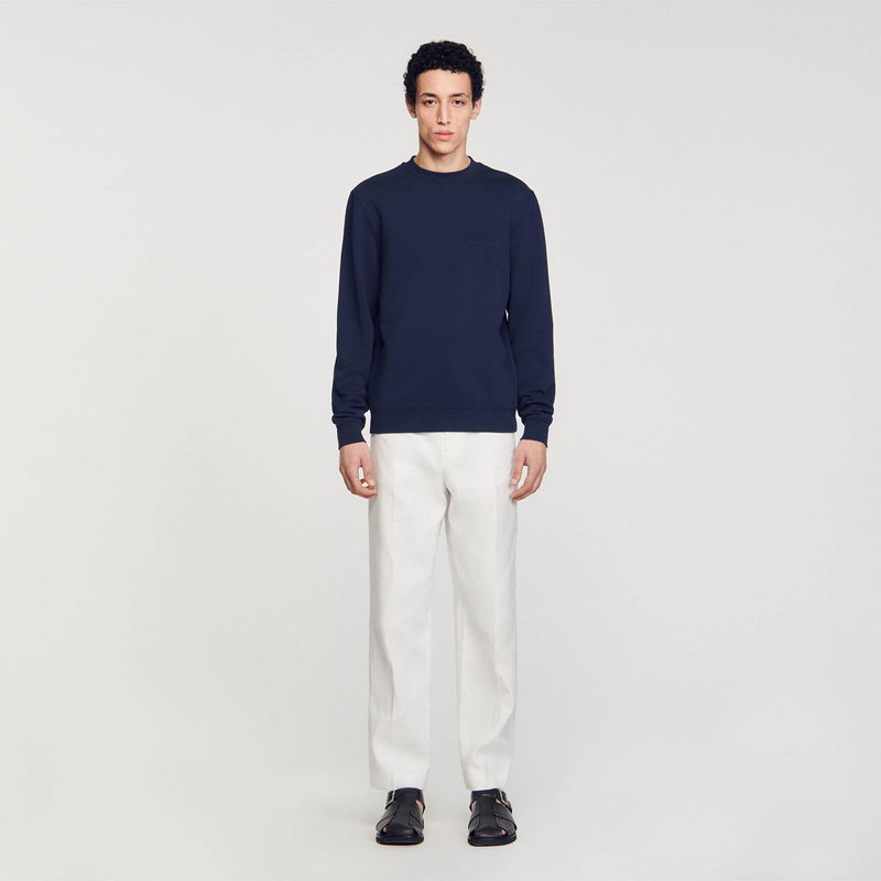 Man wearing a textured navy sweatshirt and cream trousers.