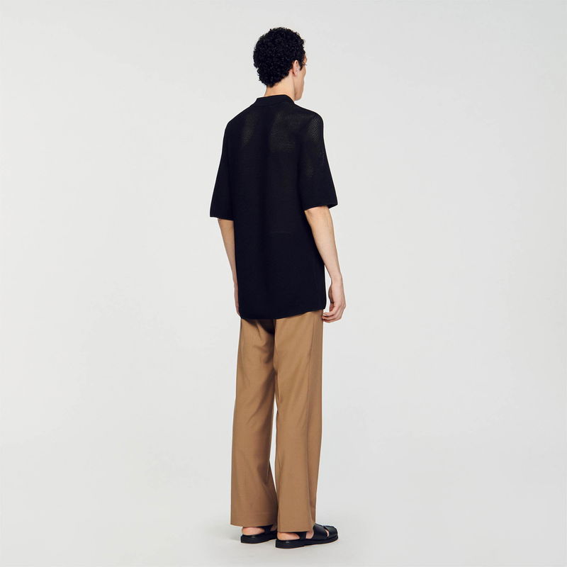 Black mesh short-sleeve top and tan trousers with sandals.