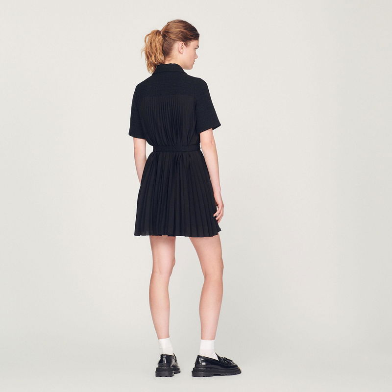 Black pleated dress with a belted waist, worn by a model.