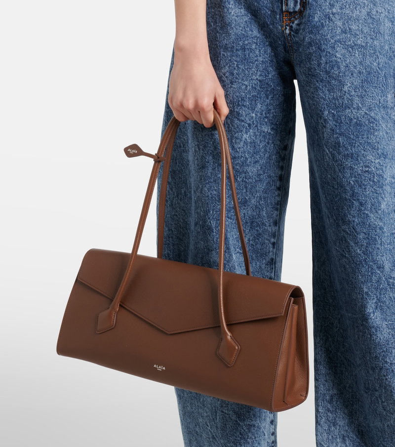 Brown leather tote bag held by a woman.