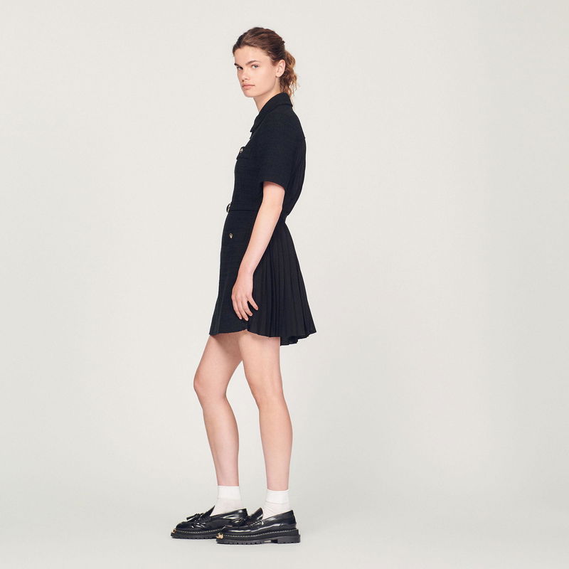 Black pleated dress with gold buttons, worn by a model.
