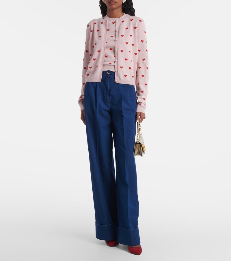 Pink cardigan with heart embroidery, paired with wide-leg navy trousers and a gold handbag.