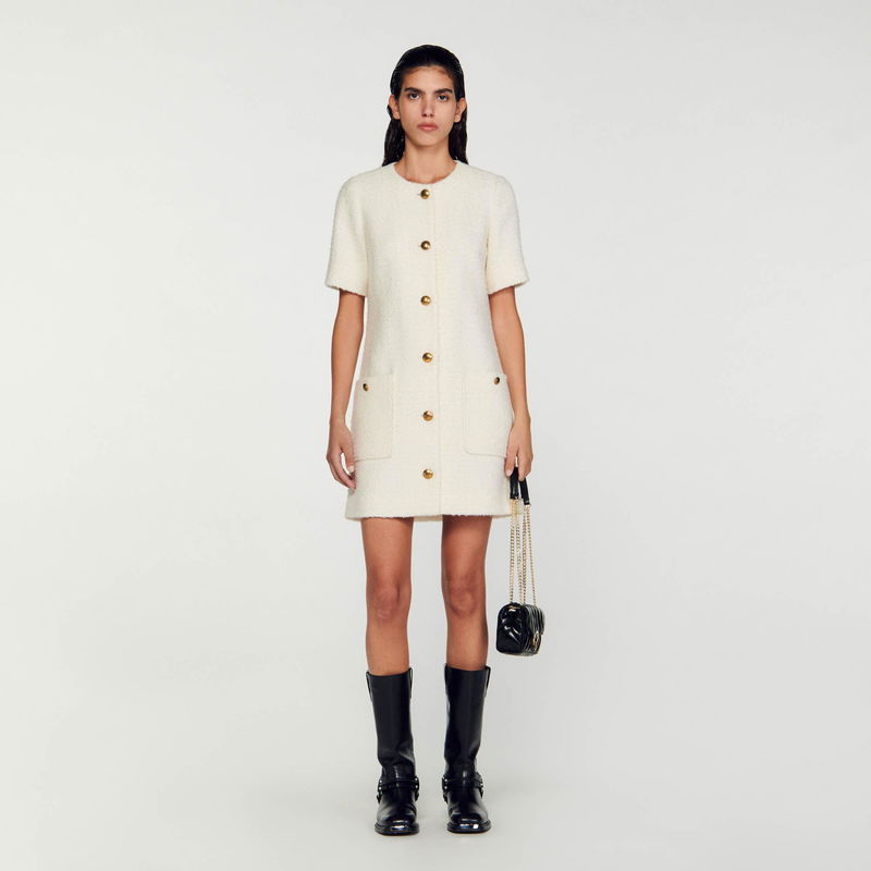Cream-colored tweed dress with gold buttons, worn by a woman.