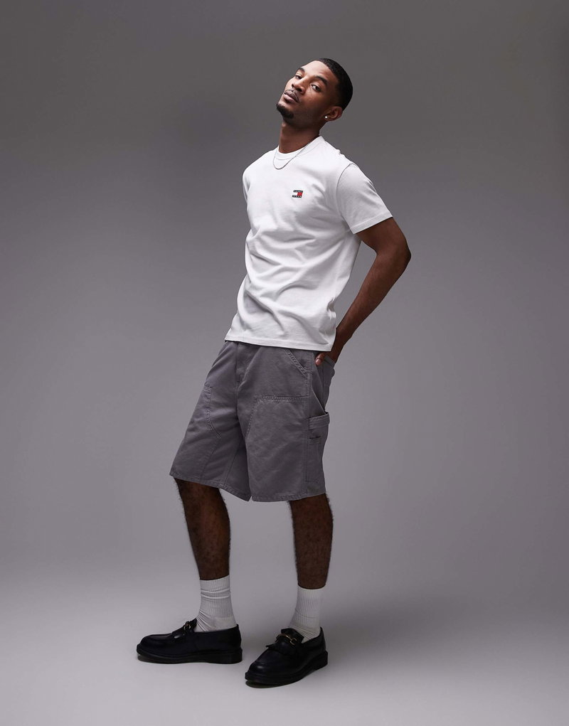 Tommy Jeans man in white tee and grey cargo shorts, posing casually against a grey background.