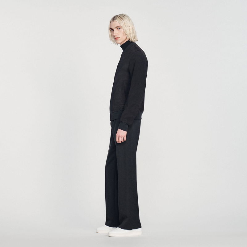 Sandro model wearing a black zip-up jacket and wide-leg trousers.