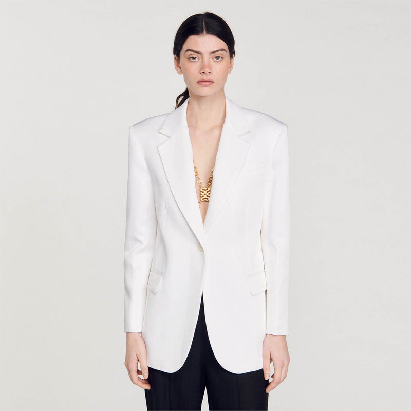 White blazer with gold chain detail, featuring a model.