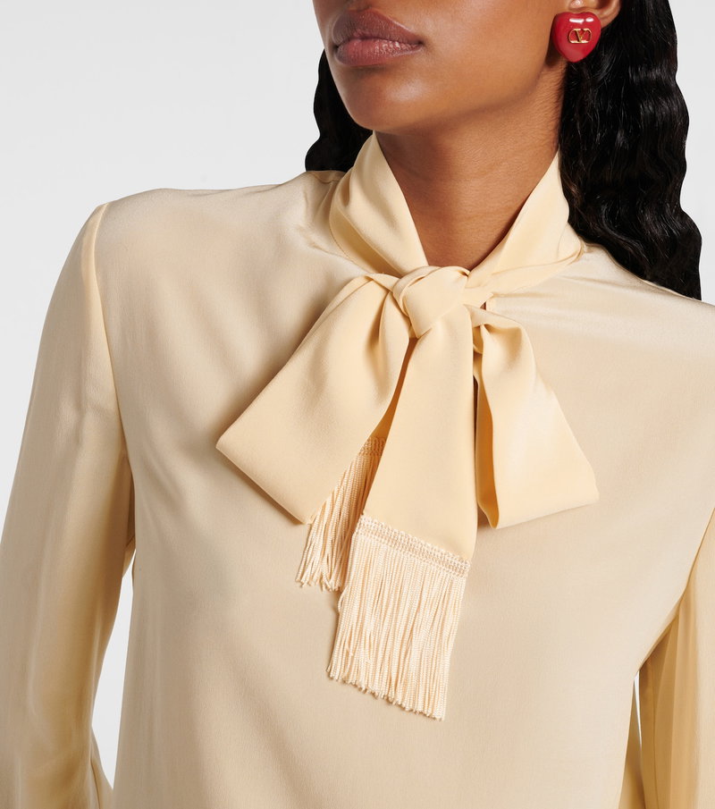 Valentino satin blouse with a cream-colored bow and fringed detail, featuring a model wearing red Valentino earrings.