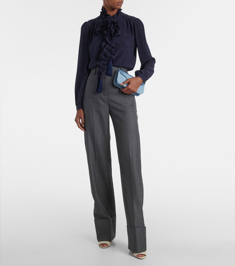Navy silk blouse with ruffled neckline, paired with gray trousers and a blue clutch.