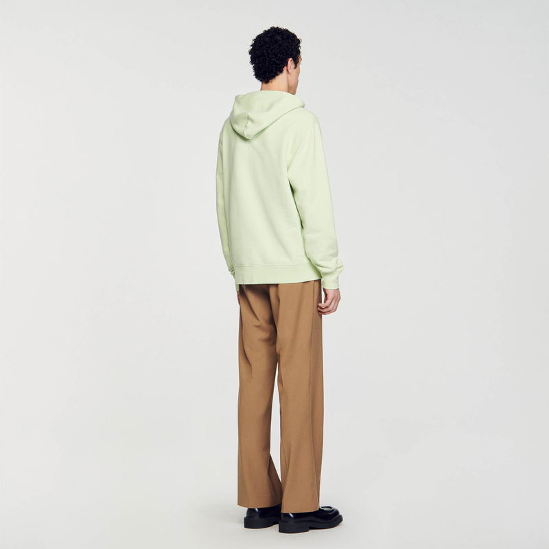Sandro man wearing a pale green hoodie and brown trousers.