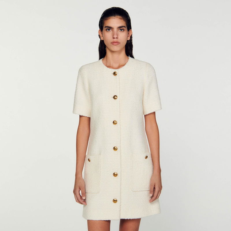 Cream-colored tweed dress with gold buttons, worn by a woman.
