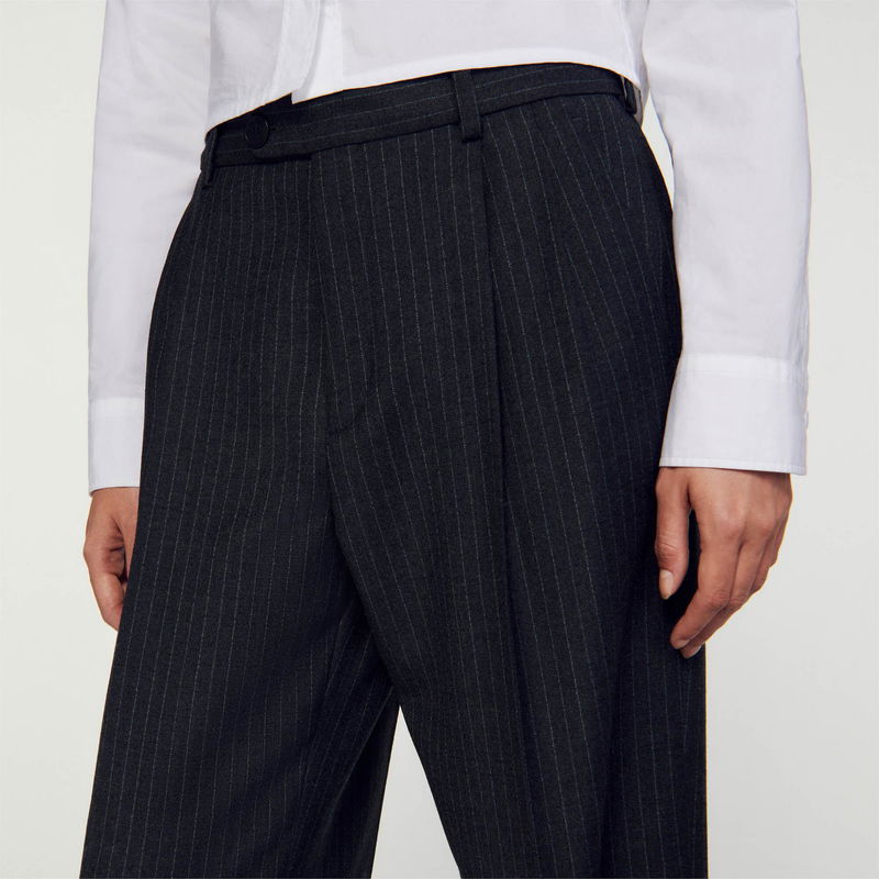 Dark pinstripe trousers with pleats, worn by a person.
