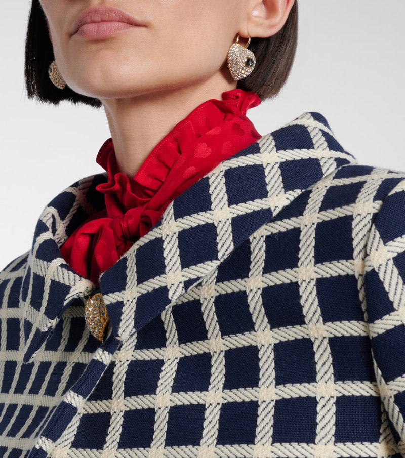 Close-up of a woman wearing Valentino's diamond-studded earrings and a patterned, ruffled blouse with a blazer.