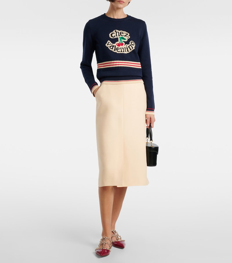 Navy sweater with cherry and Valentino logo, paired with a pale beige midi skirt and studded heels.