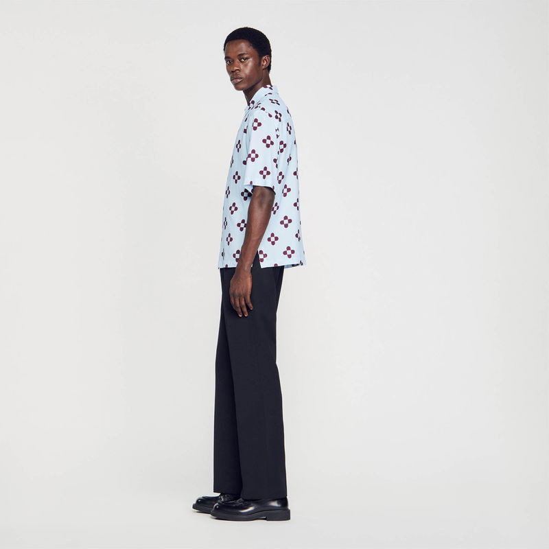 SANDRO - Man in light blue shirt with floral pattern, wearing black trousers and shoes.