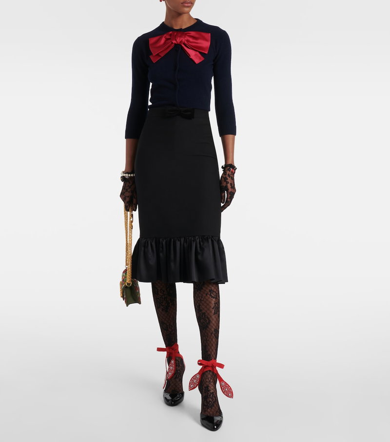 Valentino model wearing a navy sweater with a red bow, black pencil skirt with a ruffled hem, lace gloves, and red heels.