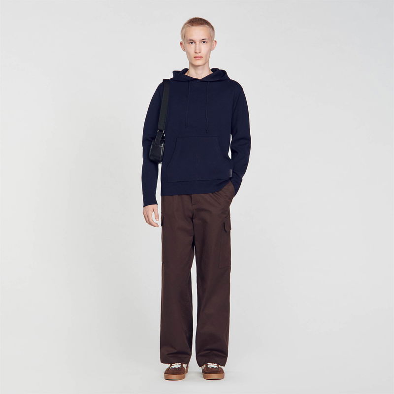 Man wearing a navy hooded sweatshirt, brown cargo pants, and brown shoes.