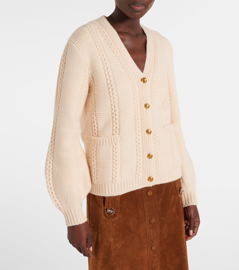 Cream cable-knit cardigan with gold buttons, worn over a brown suede skirt.