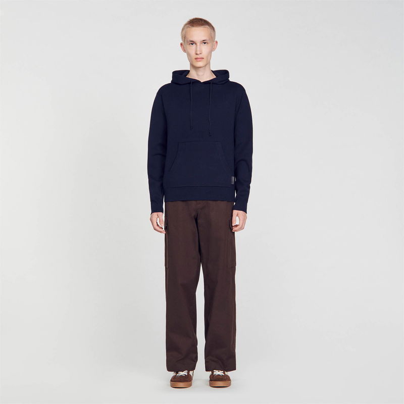 Dark blue hooded sweatshirt worn by a man, with brown trousers.