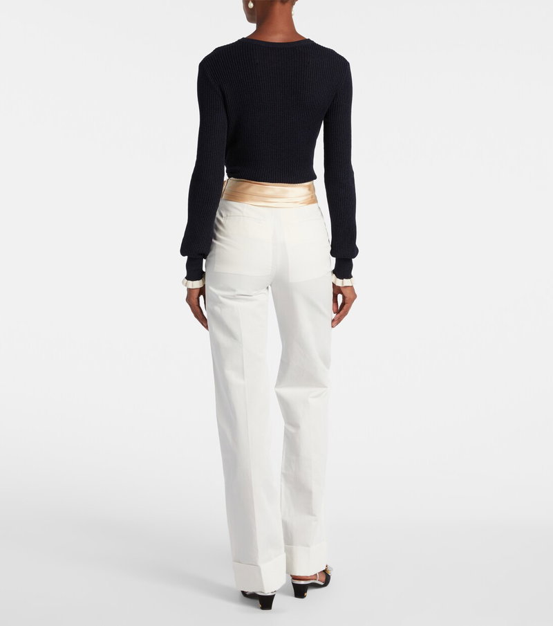 Black ribbed sweater with gold trim, paired with wide-leg trousers.