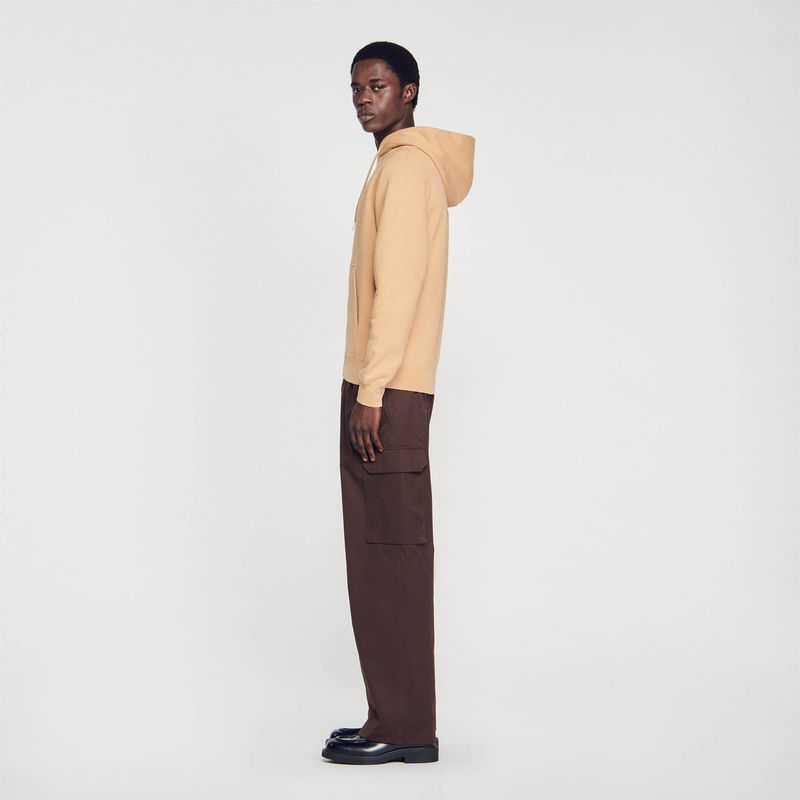 Sandro man wearing a beige hoodie and brown trousers.