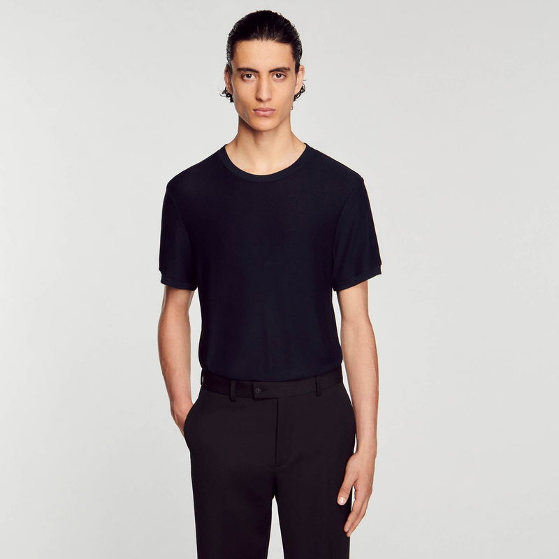 Man wearing a black t-shirt and trousers against a white background.