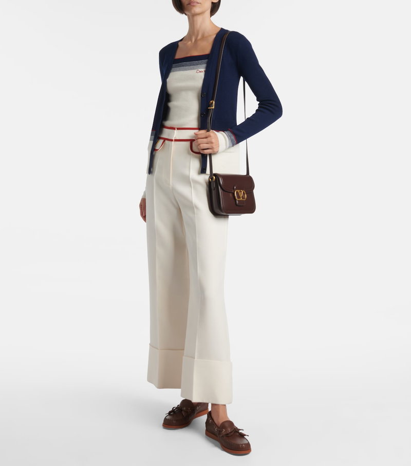 Valentino woman wearing a cream sweater, navy cardigan, and brown crossbody bag.
