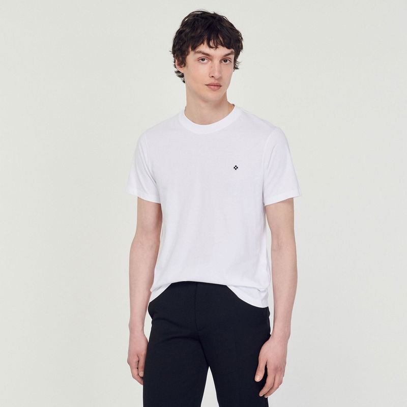 Sandro white t-shirt with black trousers, featuring a small embroidered logo.