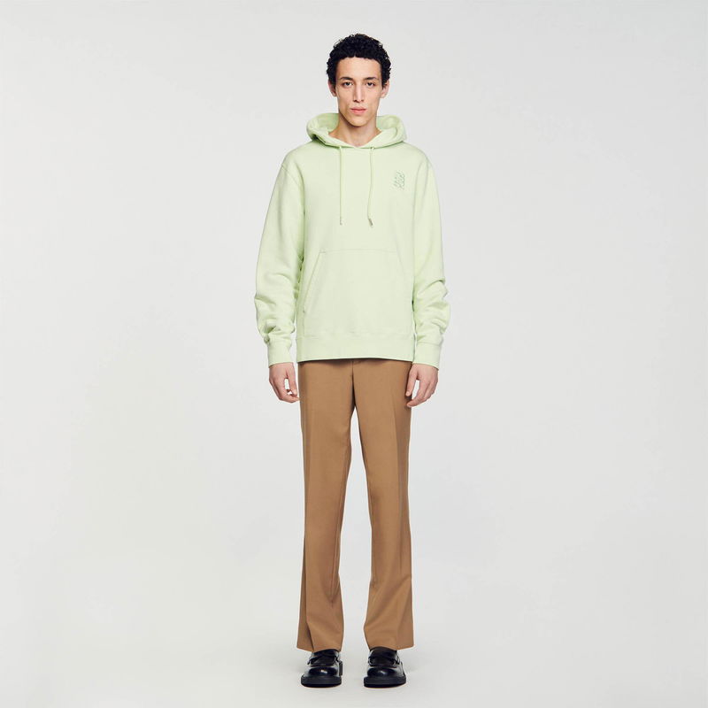 Pale green SANDRO hoodie with embroidered logo, worn by a young man with brown trousers and shoes.