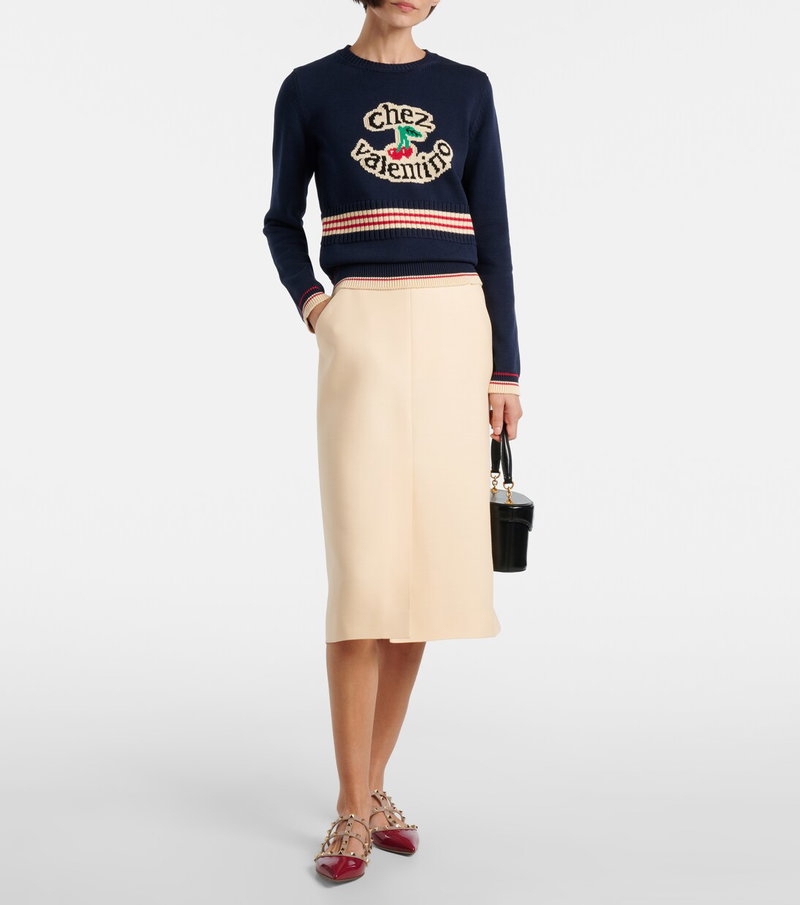 Valentino navy and red sweater with cherries and chez Valentino embroidery, paired with a cream pleated skirt and red Valentino heels.