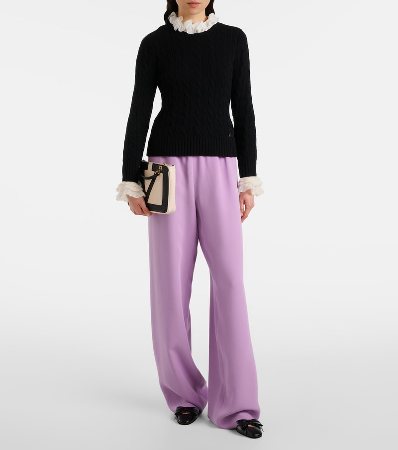 Black cable-knit sweater with ruffled trim and lilac wide-leg trousers.
