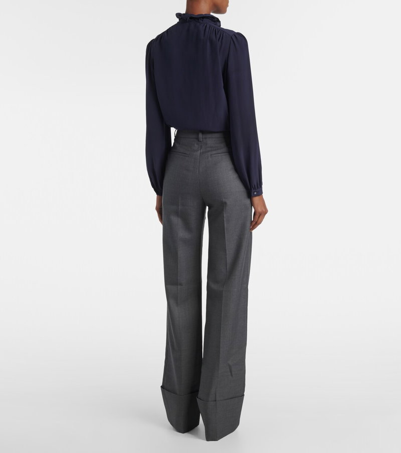 Navy silk blouse with ruffled neckline, paired with gray trousers.