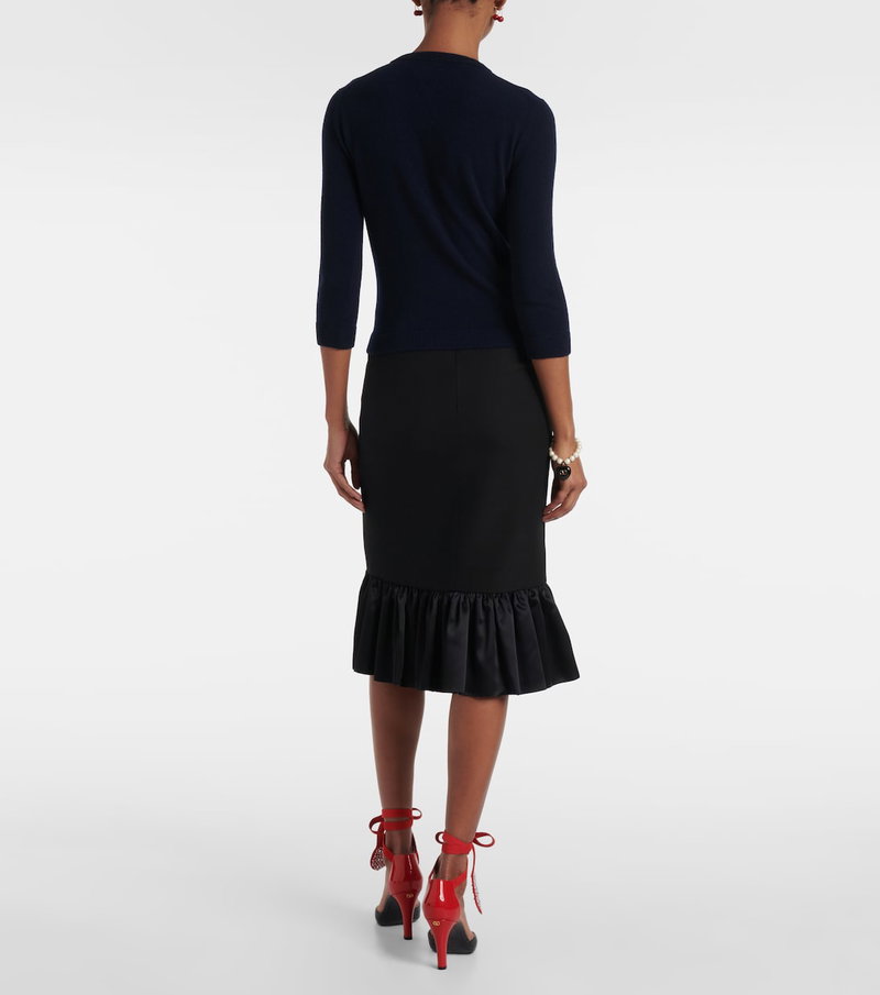 Woman wearing a navy sweater and black ruffled skirt with red heels.
